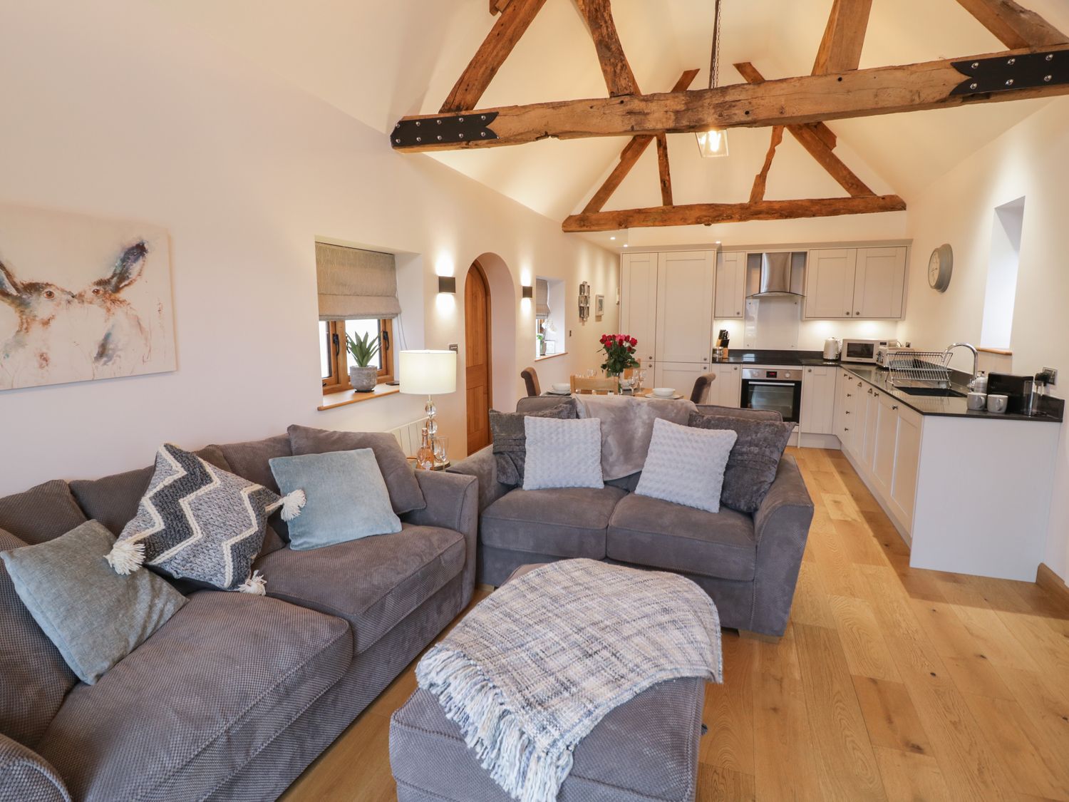 An open plan living room and kitchen with wooden beams on the ceiling sofas and a dining table at The Parlour in Droitwich Spa