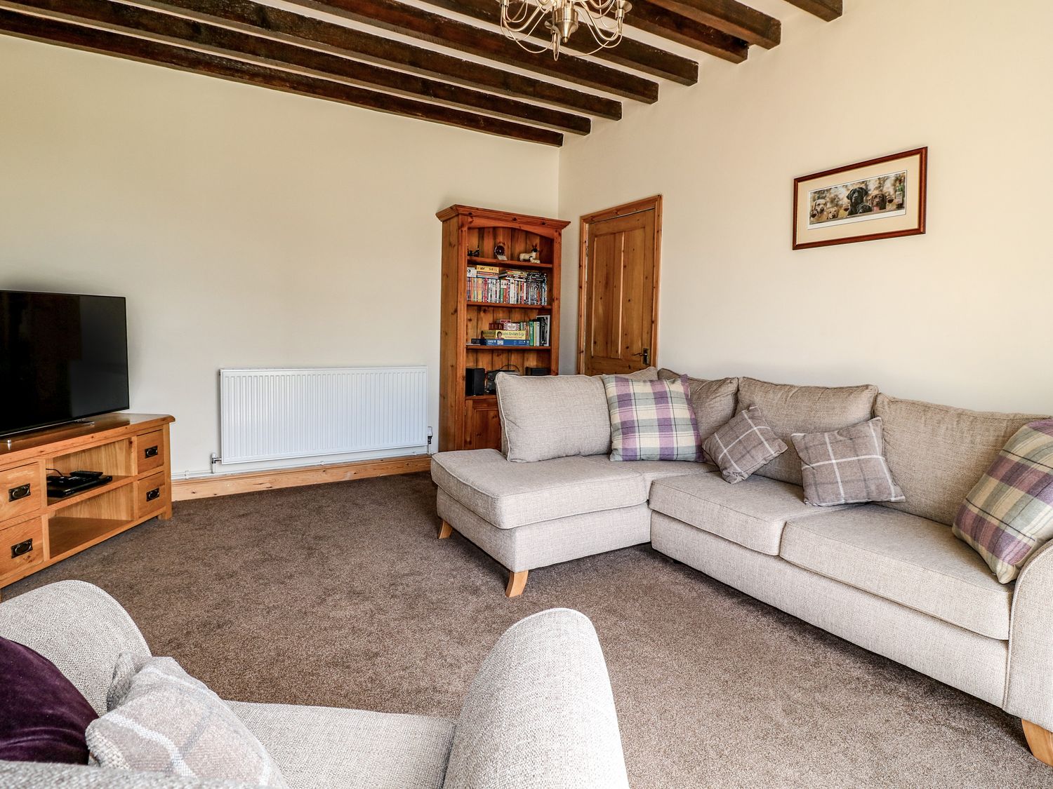 A living room with beige sofas a wooden bookshelf and a TV at Hillcrest in Cottam near Rampton