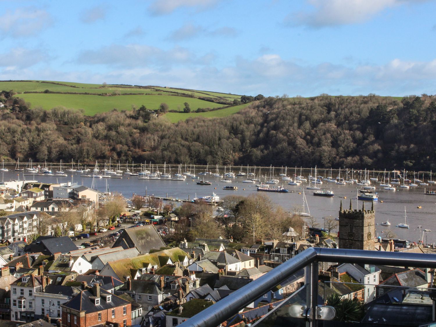 A view of a harbor with boats on the water and a town with houses and a church tower in the foreground at Windwhistle in Dartmouth