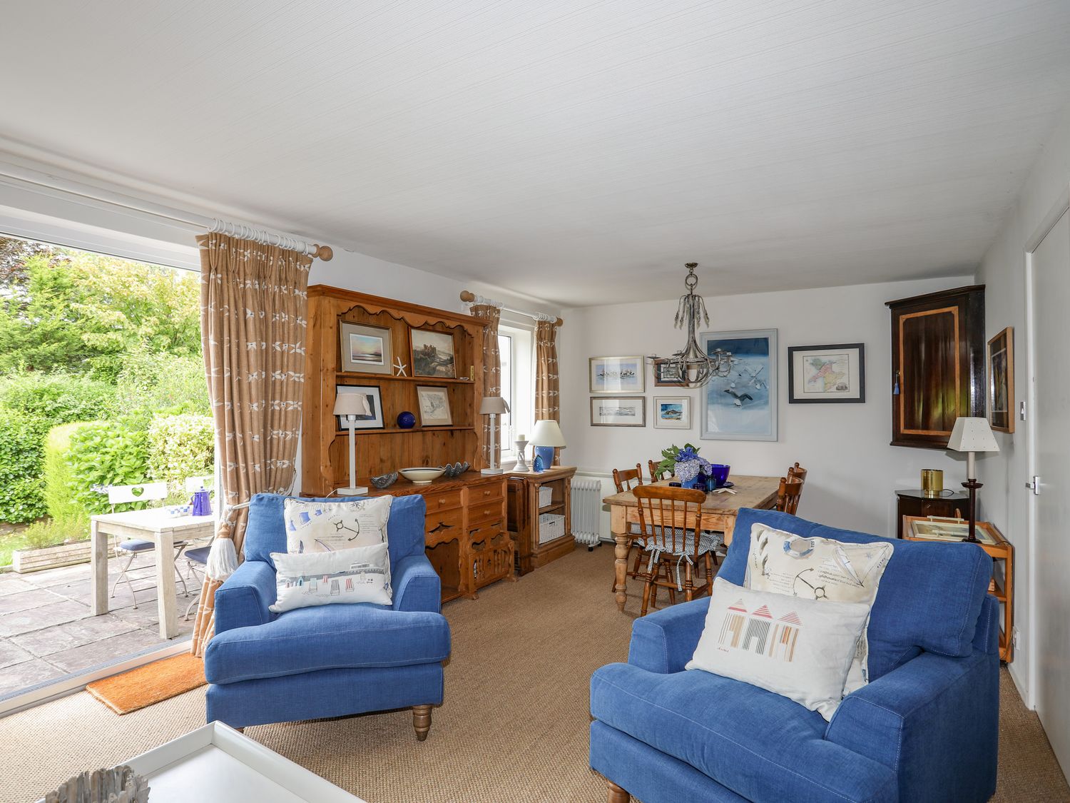 A living room with blue armchairs wooden dining table and cabinet at Llwyn Gwalch in Morfa Nefyn