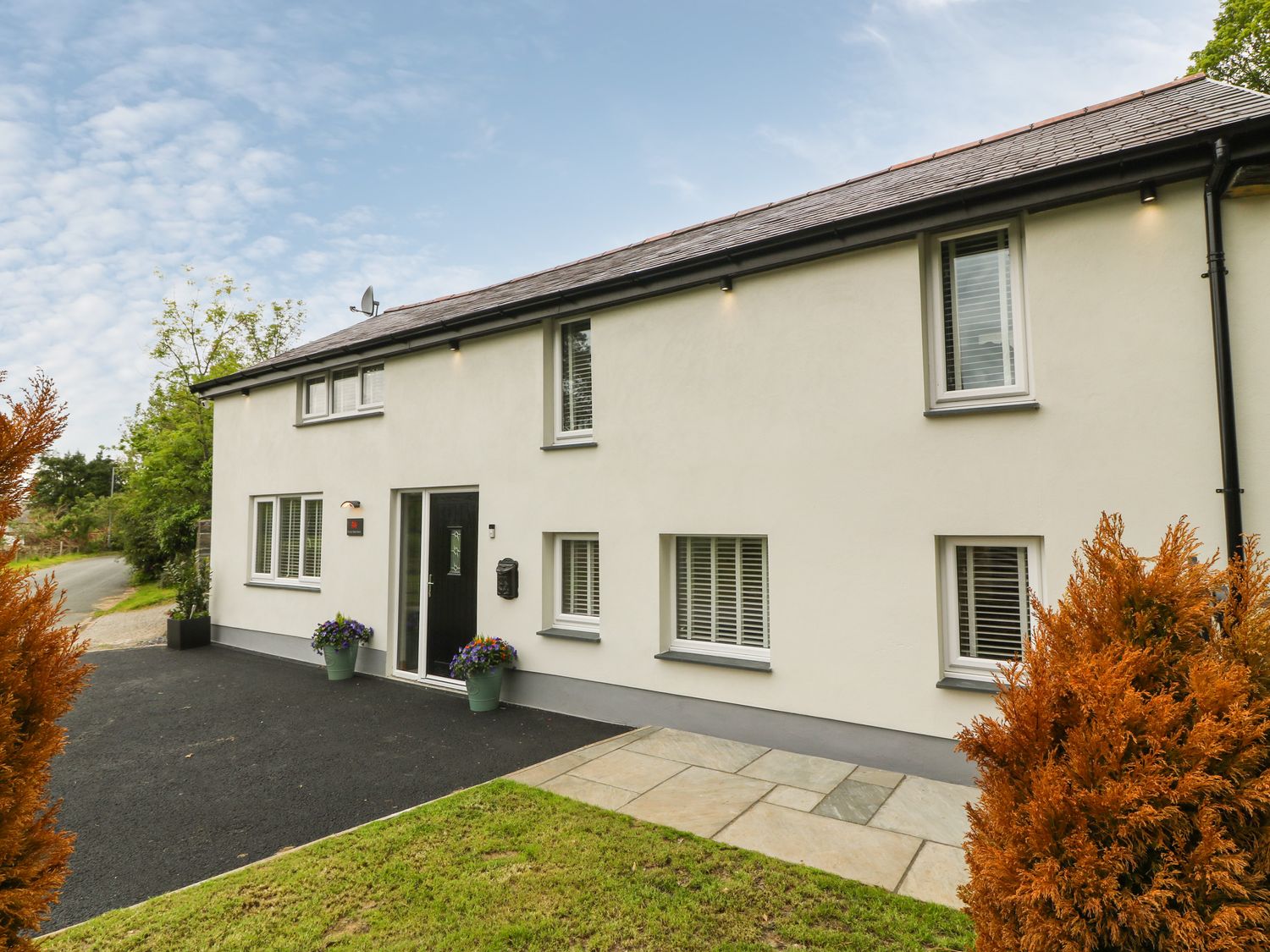The exterior of a two story house with multiple windows a black front door flower pots and a paved walkway at Bwthyn Bach Gwyn in Penrhyndeudraeth