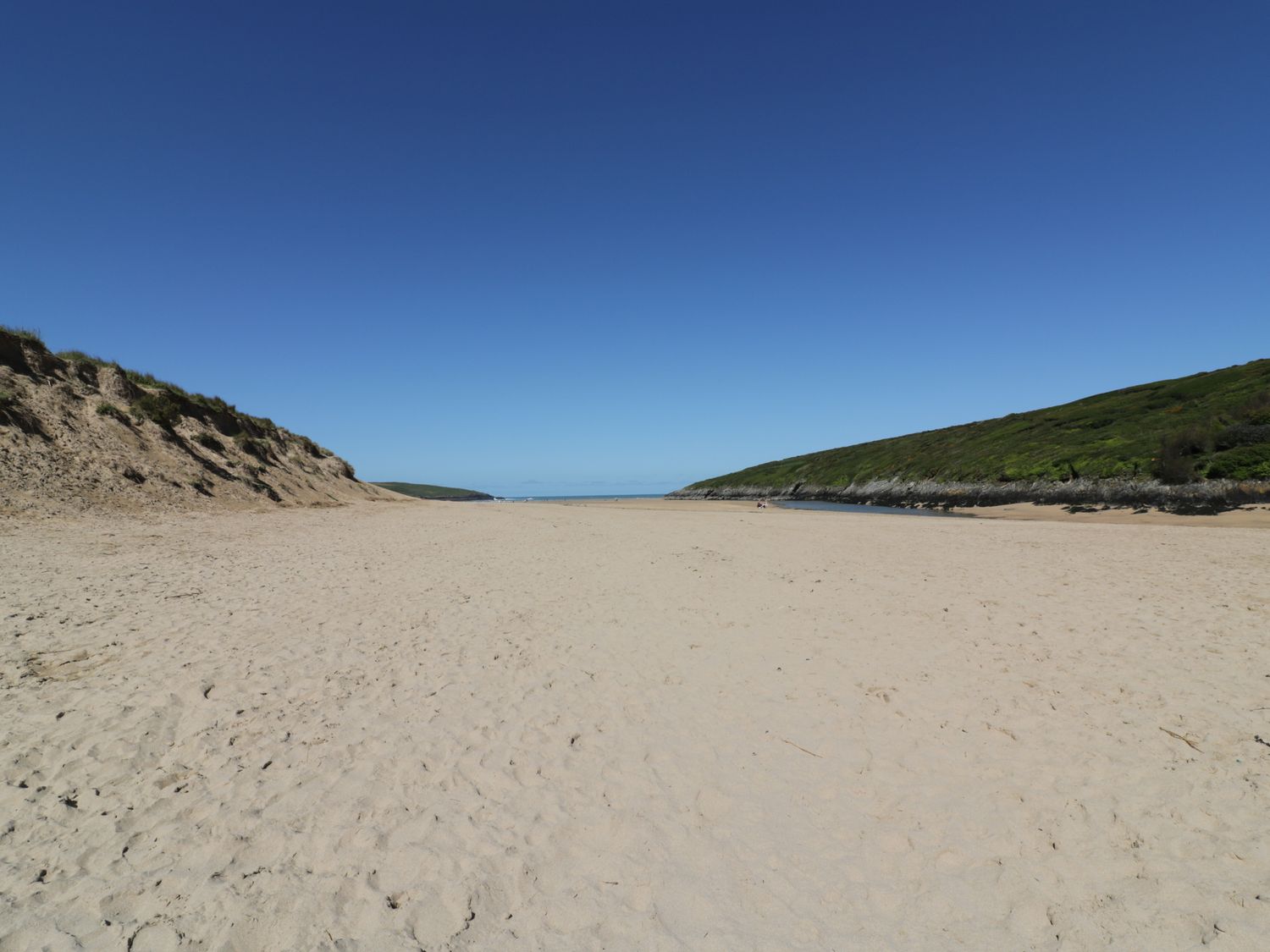 A sandy beach between grassy dunes under a clear blue sky at Great Western Farmhouse in Crantock