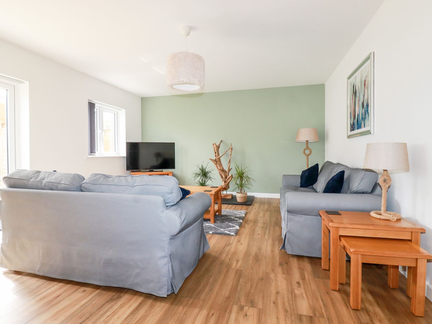 A living room with two gray sofas and wooden tables with lamps and TV at Penn-An-Vownder in Quintrell Downs