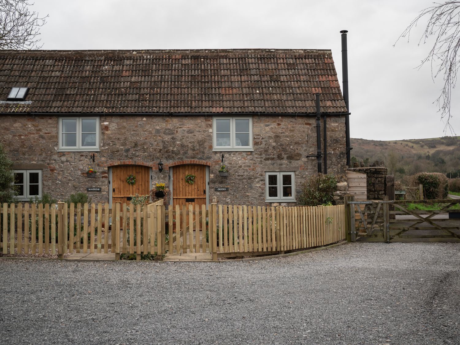 A stone cottage with two wooden doors and a picket fence at Crooks in Axbridge
