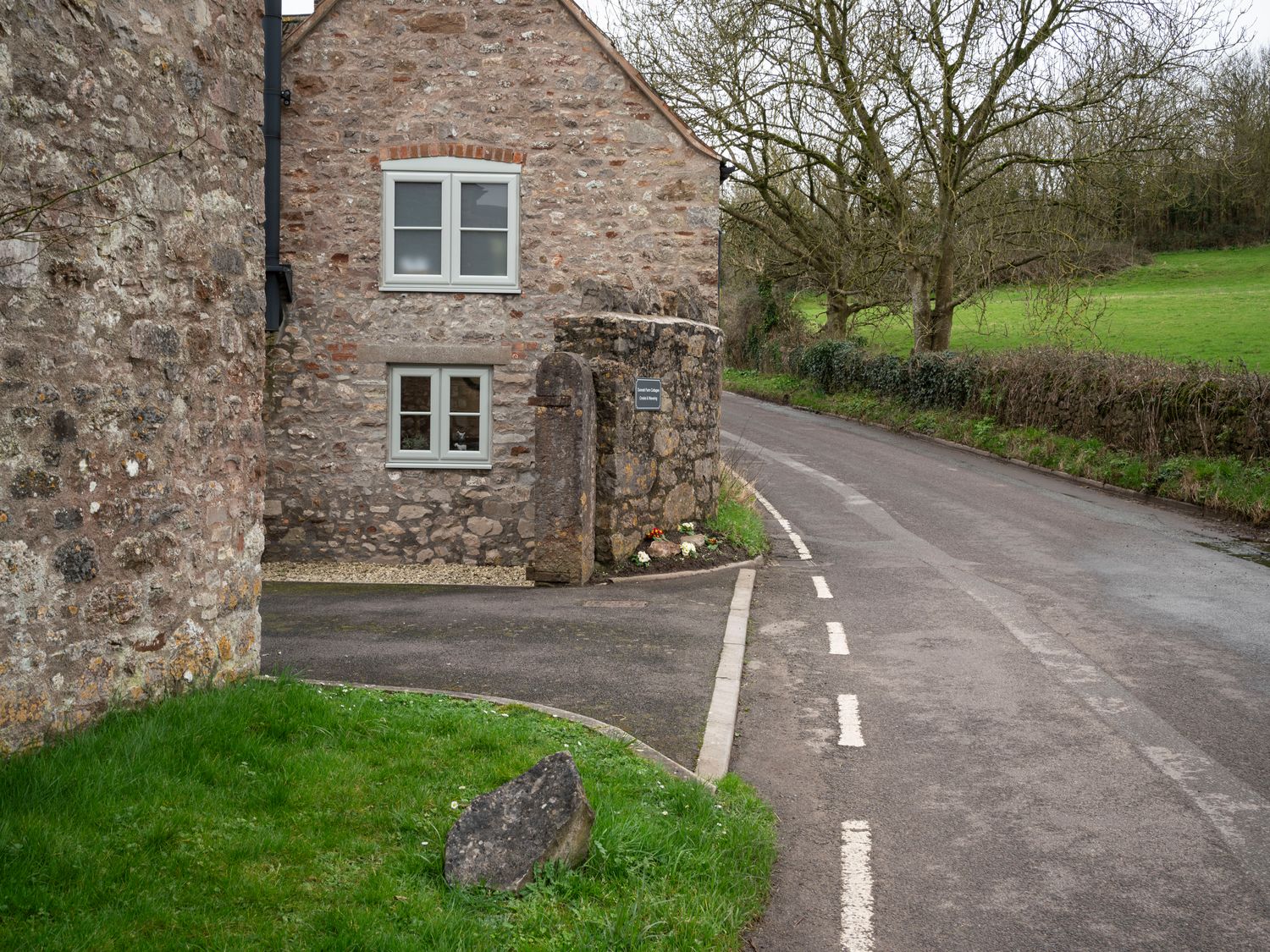 A stone cottage next to a road with grass and trees in the background at Crooks in Axbridge