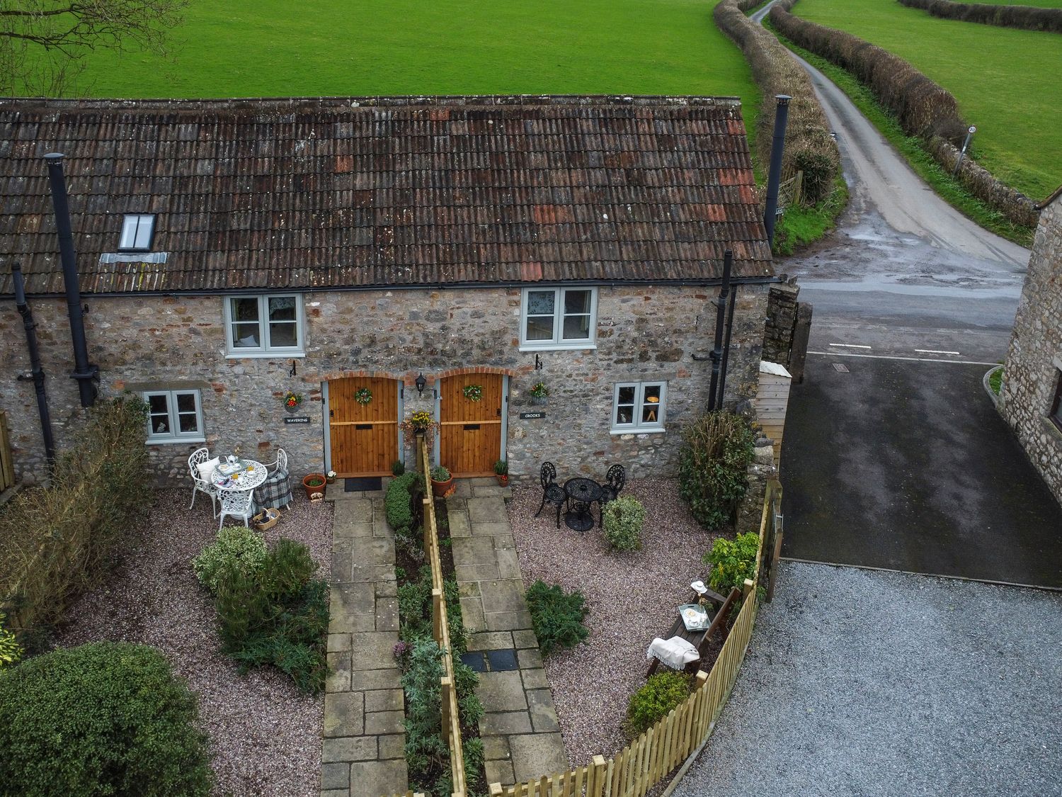 A stone cottage with two wooden doors and outdoor seating areas in front at Crooks in Axbridge