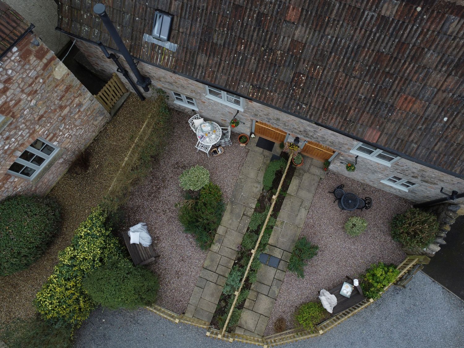 An aerial view of a courtyard with two wooden doors stone pathways bushes tables and chairs at Crooks in Axbridge