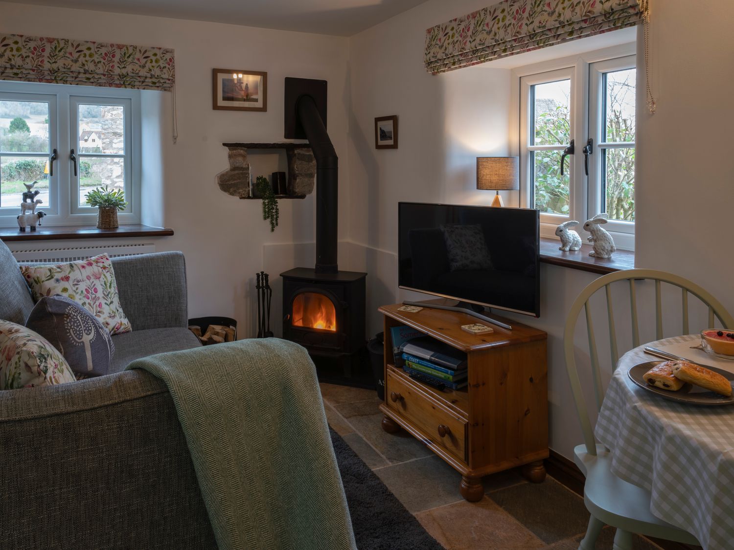 A living room with a sofa a wood burning stove a television on a wooden stand and a dining table at Crooks in Axbridge
