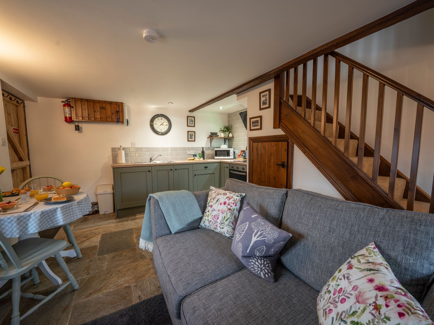 A small kitchen and dining area with green cabinets a gray sofa and wooden stairs at Crooks in Axbridge