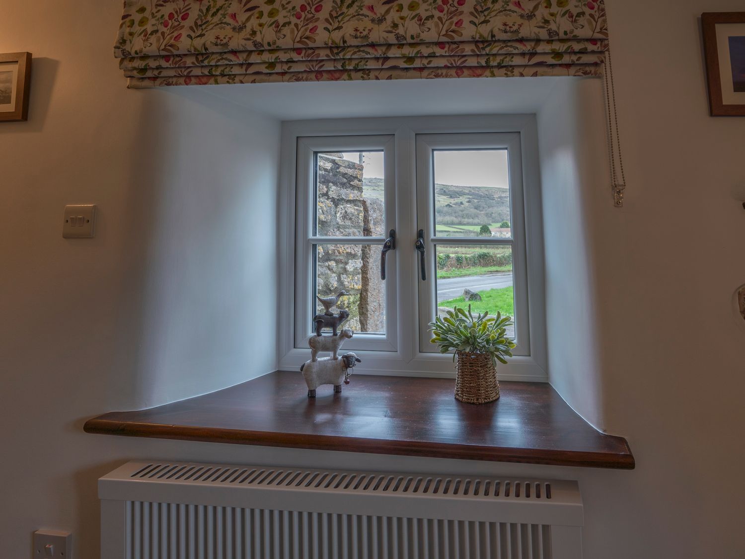 A window with floral blinds a wooden windowsill with animal figurines and a plant at Crooks in Axbridge