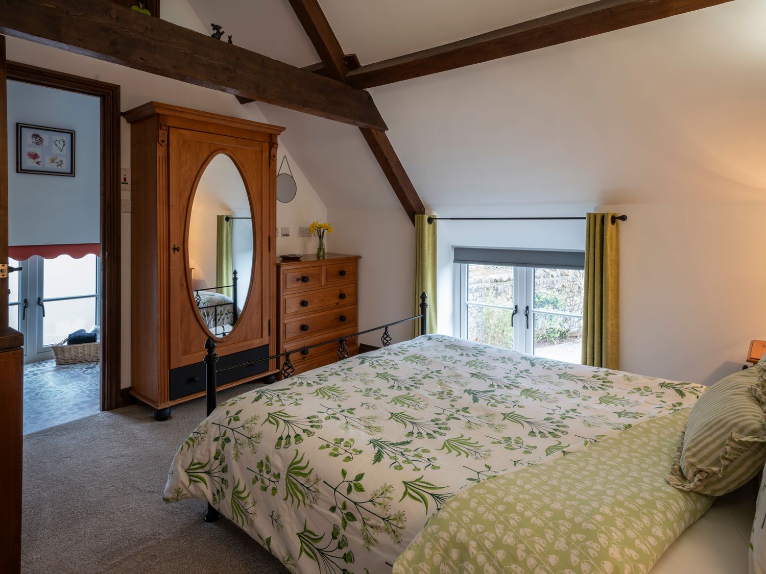 A bedroom with a bed covered in floral bedding a wooden wardrobe with a mirror and a chest of drawers at Crooks in Axbridge