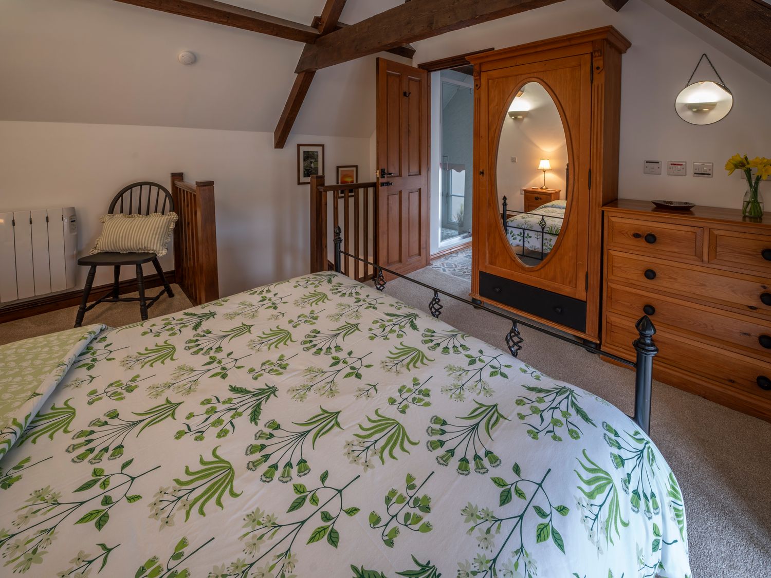 A bedroom with a bed with floral bedding a wooden wardrobe with a mirror a chest of drawers a chair and wooden beams at Crooks in Axbridge