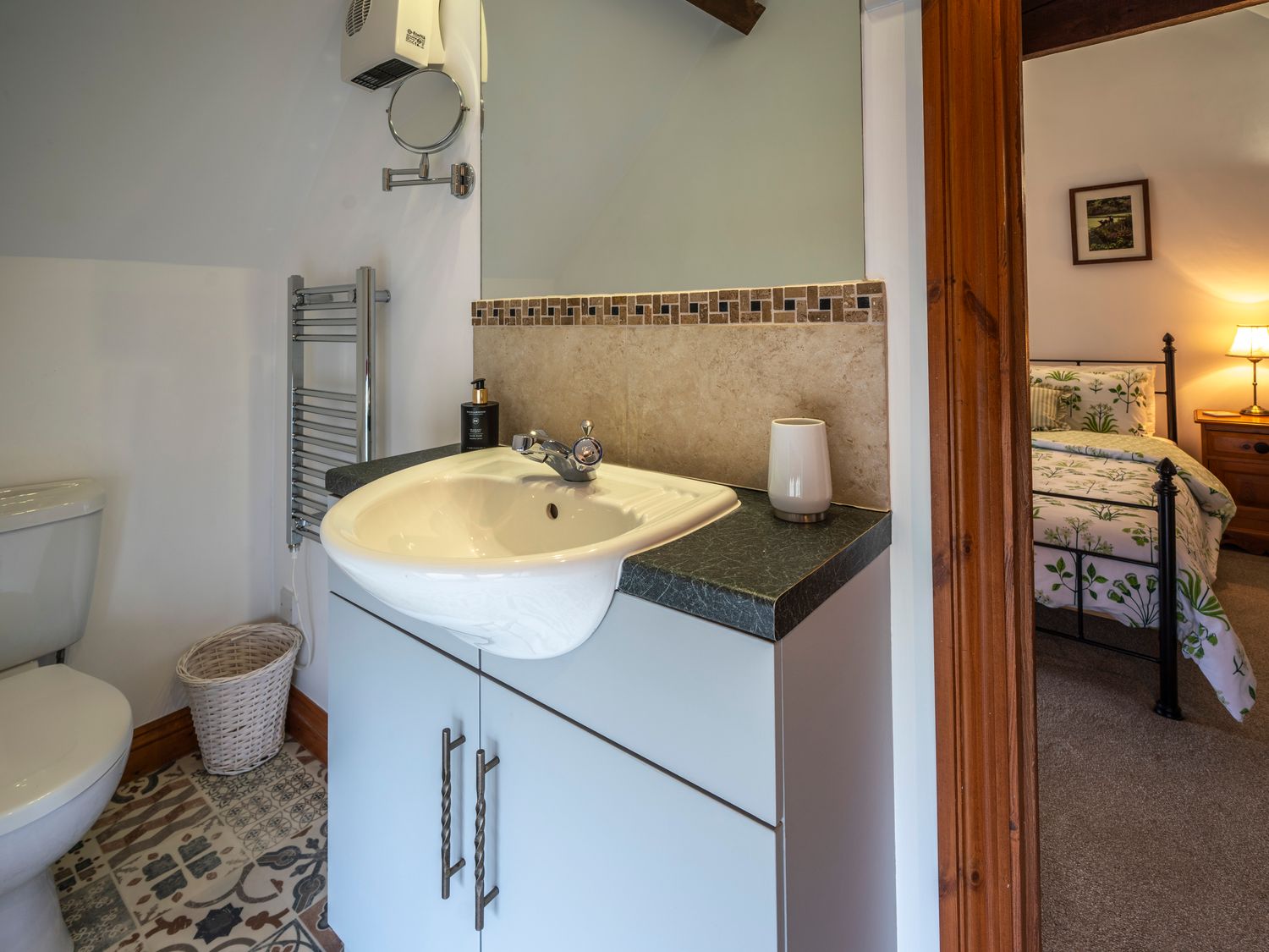 A bathroom with a white sink on a cabinet next to a toilet and a bedroom visible through a wooden door frame at Crooks in Axbridge