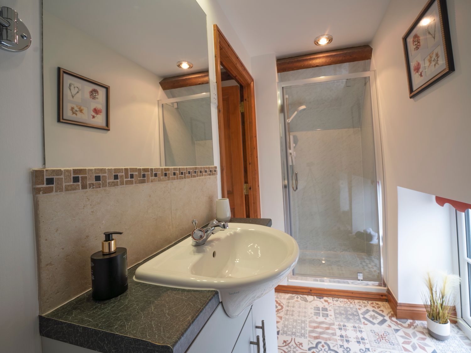 A bathroom with a sink a mirror a shower and framed pictures on the wall at Crooks in Axbridge