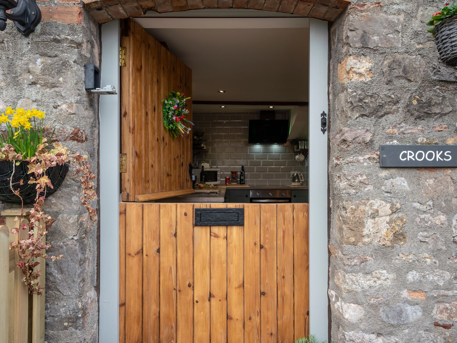A kitchen with wooden stable door and stone exterior wall with flowers at Crooks in Axbridge