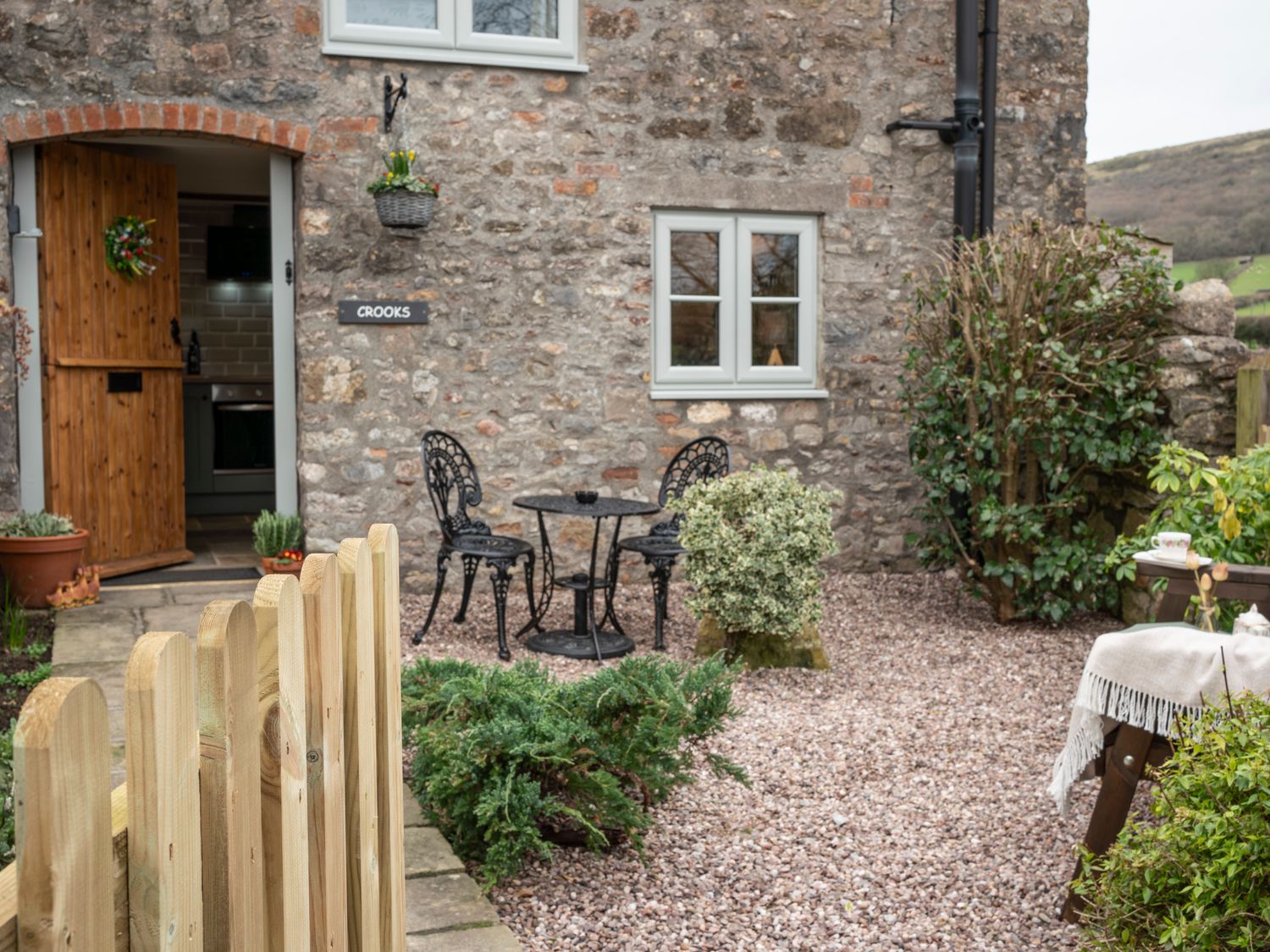 An outdoor seating area with two black metal chairs and a table outside a stone house at Crooks Axbridge