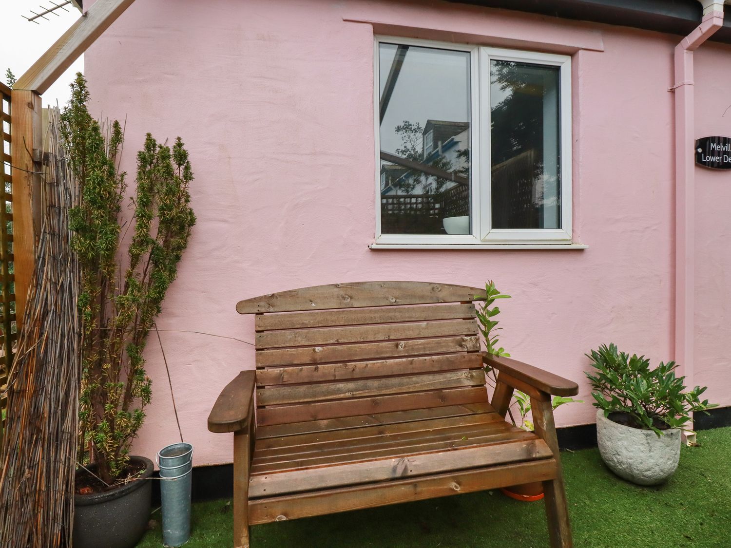 A wooden bench outside a pink building with a window and plants in pots at Melvill Lower Deck in Falmouth