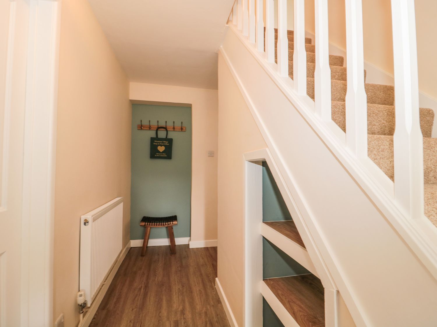 A hallway with wooden flooring a small stool a coat rack and carpeted stairs at Ammerham Farm Cottage in Ammerham near Winsham