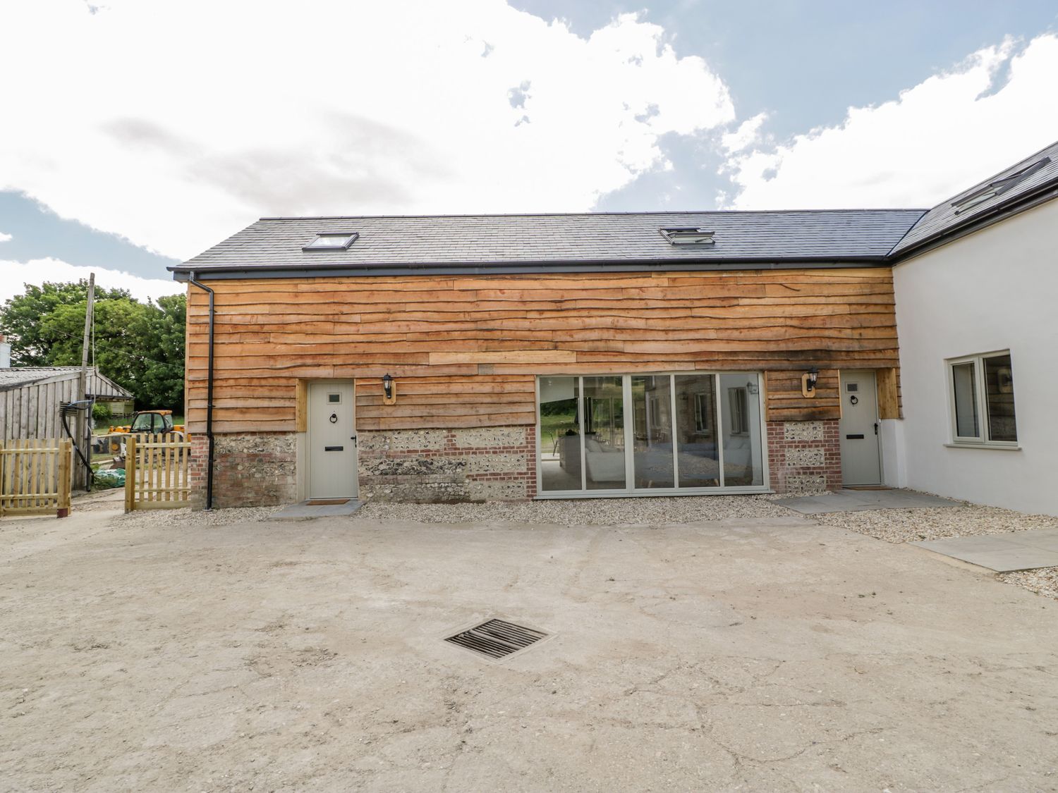 The exterior of a building with wooden siding brick and stone base two doors and large windows at Threshing Barn in Blandford Saint Mary