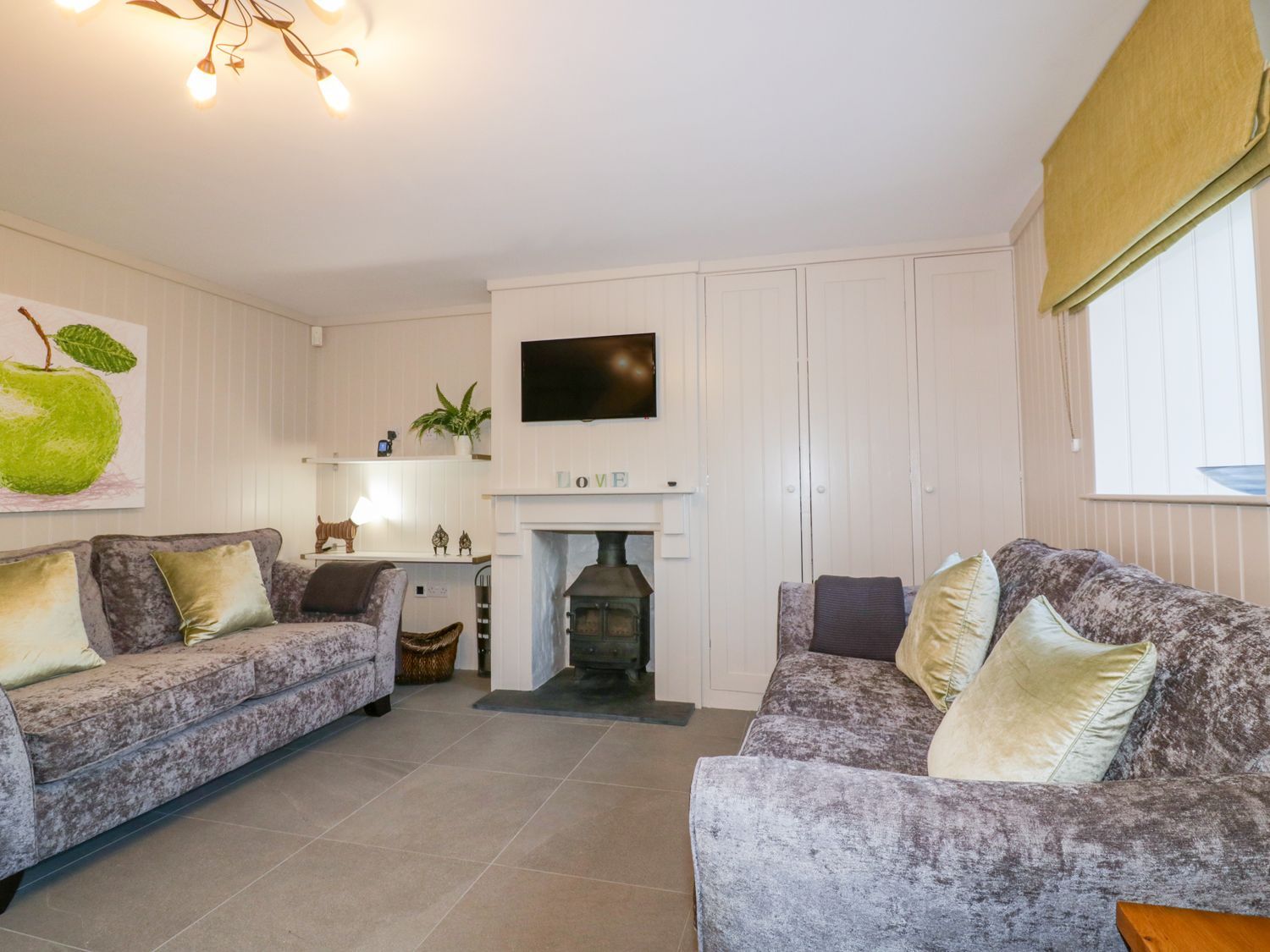 A living room with two grey sofas with green cushions a fireplace with a wood stove and a TV mounted above at Apple Barn in Crantock