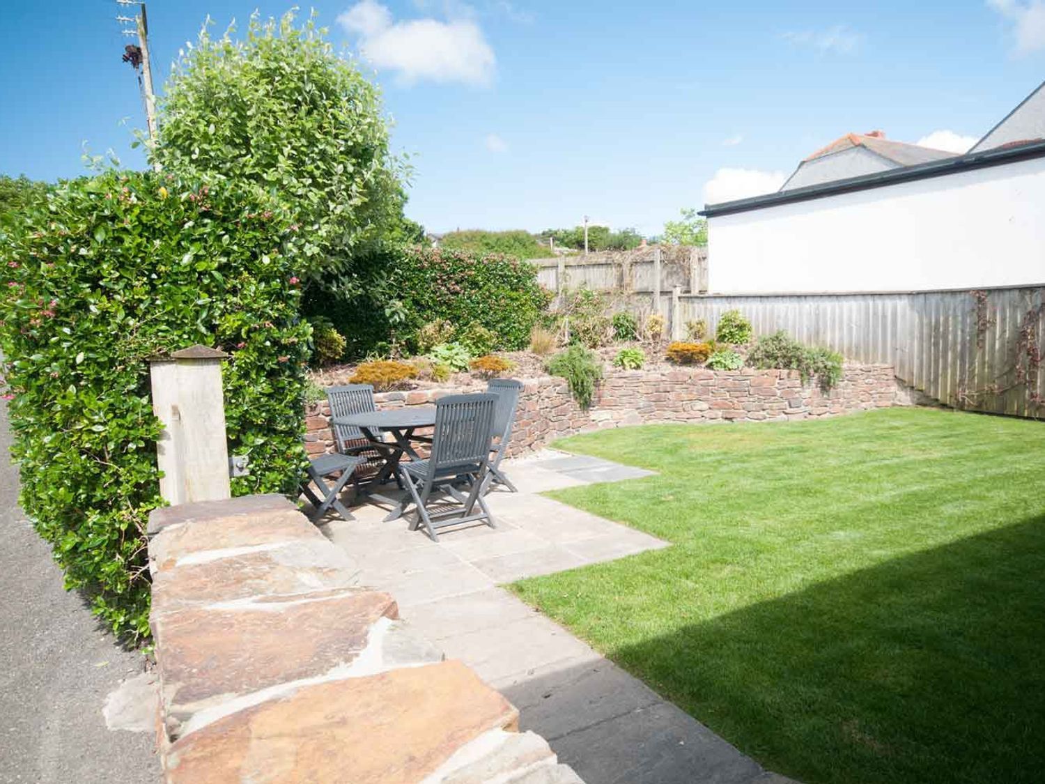 A garden with a stone patio table and chairs a stone wall and a lawn at Apple Barn in Crantock