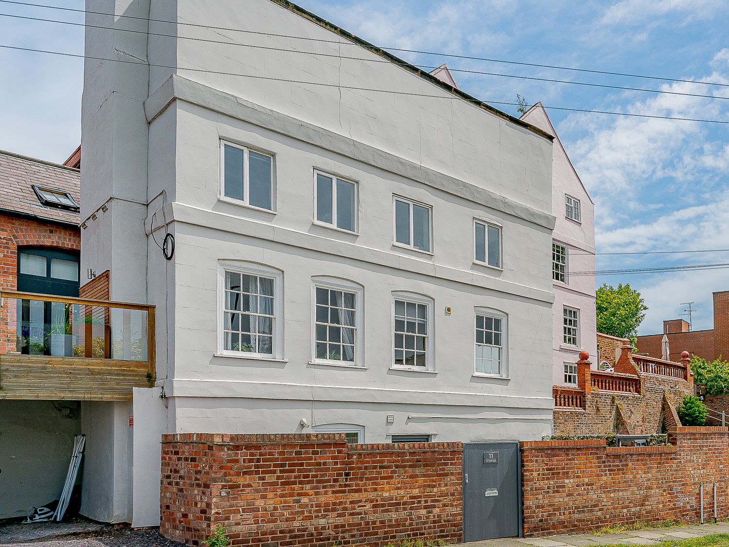 Exterior view of a white multi-storey building with windows and a brick wall with a metal gate at Ivy Cottage in Chester