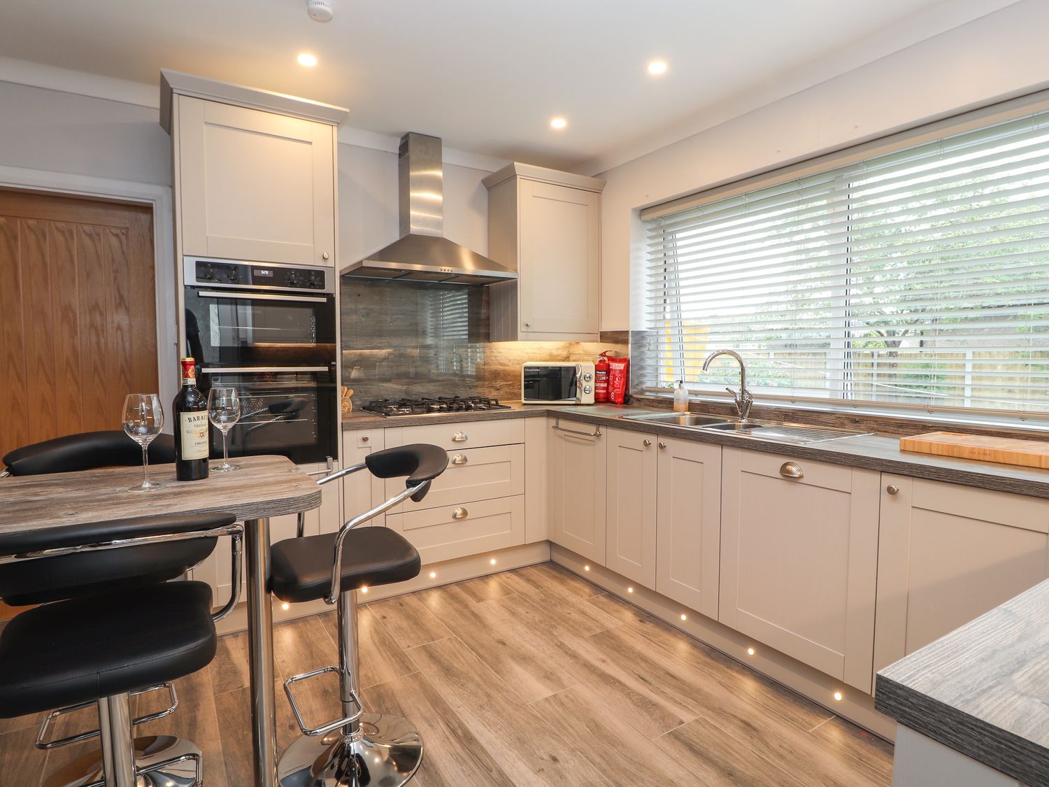 A kitchen with cabinets a stove a microwave a sink bar stools and a table at Hilltops in Deganwy