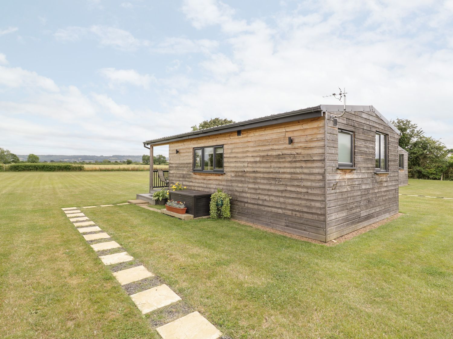 An exterior view of a wooden cabin with a pathway and grassy field at Cotswold View 3 in Bretforton near Evesham