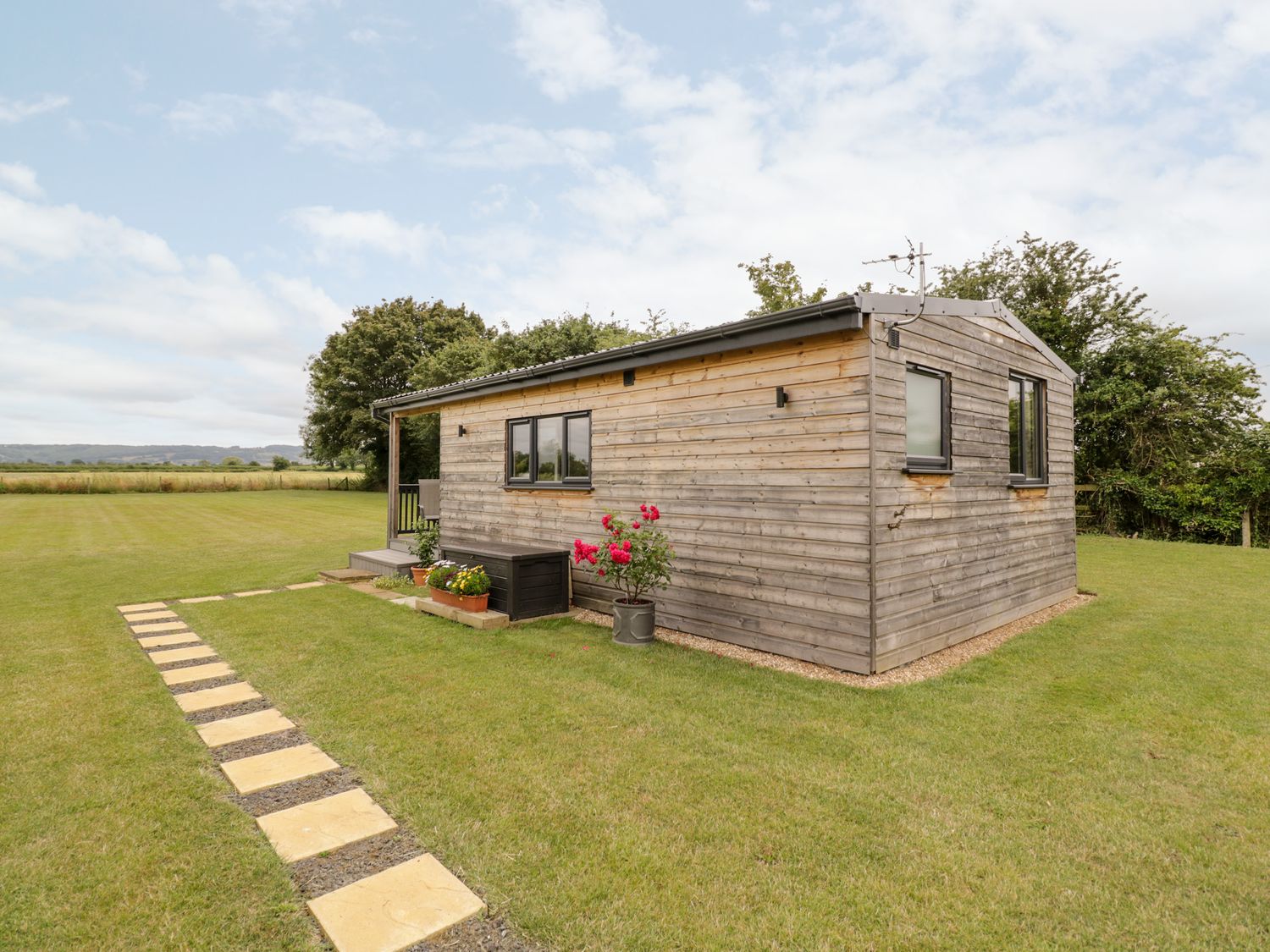 A small wooden cabin with windows and flowers on grass with stone path at Cotswold View 4 Bretforton near Evesham