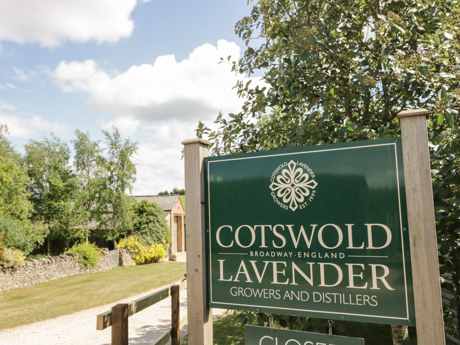A green sign for Cotswold Lavender growers and distillers next to a gravel path with trees and a stone wall in the background at Cotswold View 4 Bretforton near Evesham