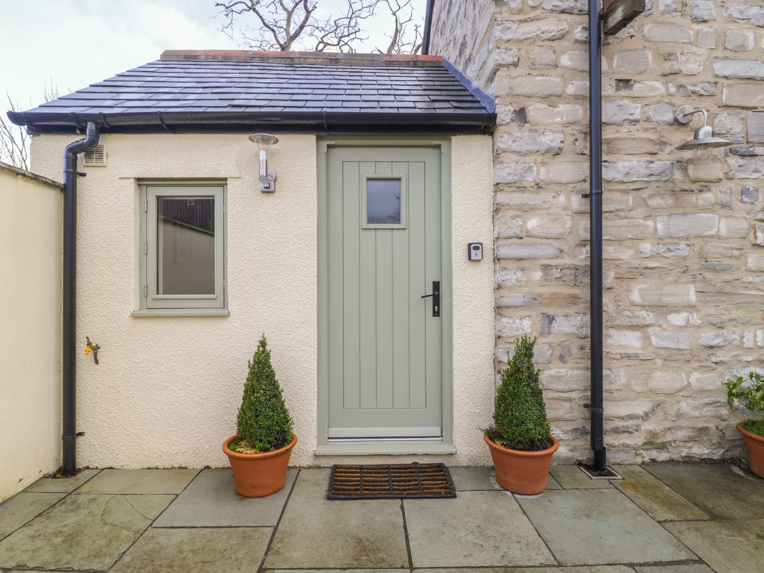 A small outdoor entrance with a green door and window flanked by two potted plants on a stone patio at Magnolia Barn in Mark