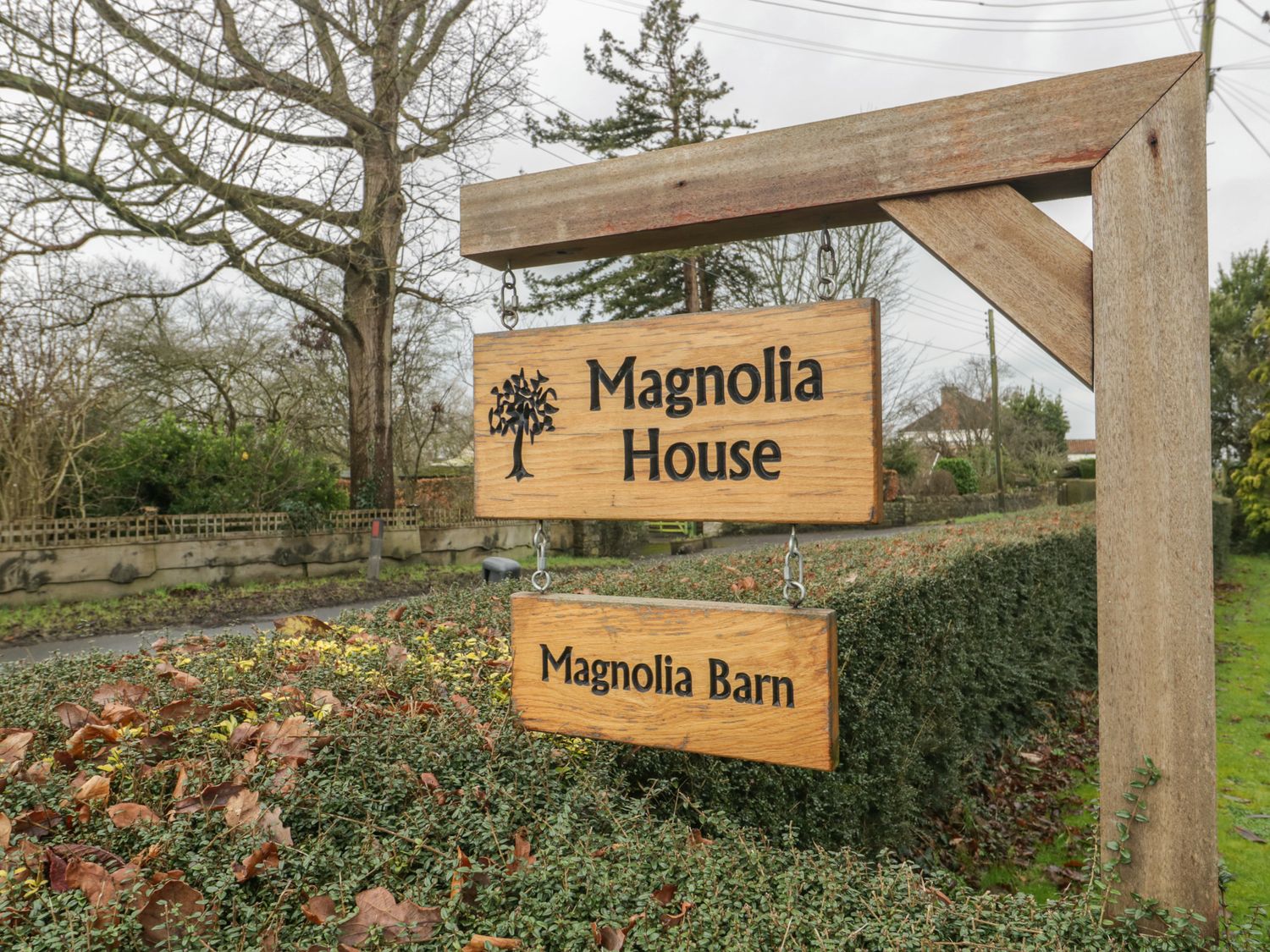 A wooden signpost with two signs reading Magnolia House and Magnolia Barn outdoors near trees and bushes at Magnolia Barn in Mark