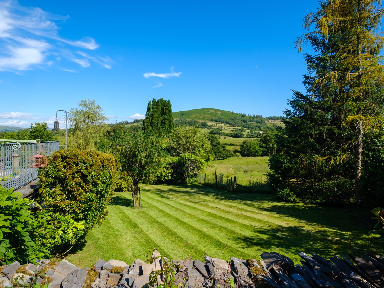 A garden with striped lawn and trees overlooking green fields and hills at Orchard Cottage in Outgate near Hawkshead