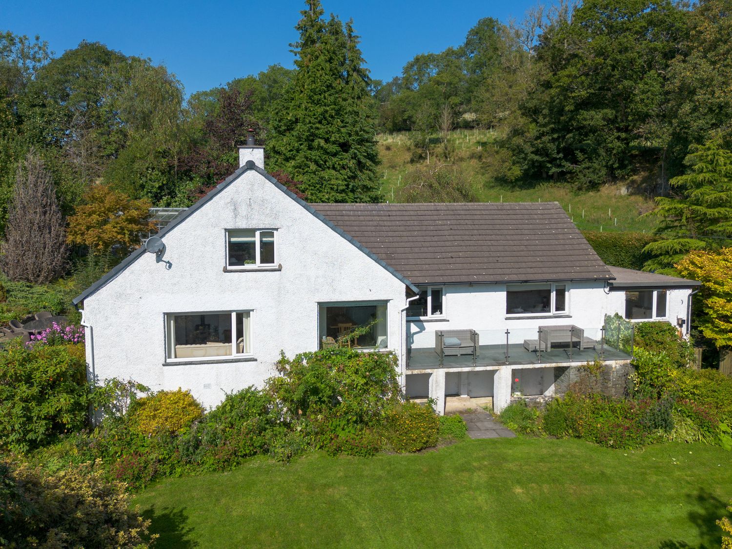A white house with a tiled roof and a balcony overlooking a garden with trees and bushes at Scarsdale in Crosthwaite
