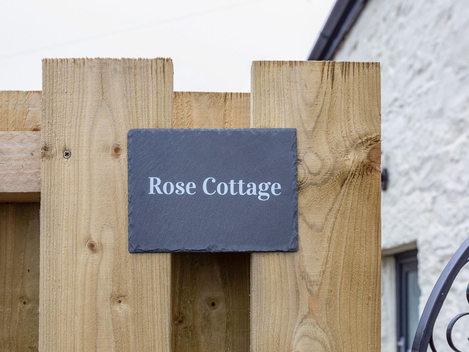 A wooden fence with a dark rectangular sign that reads Rose Cottage at Rose Cottage in St Ives