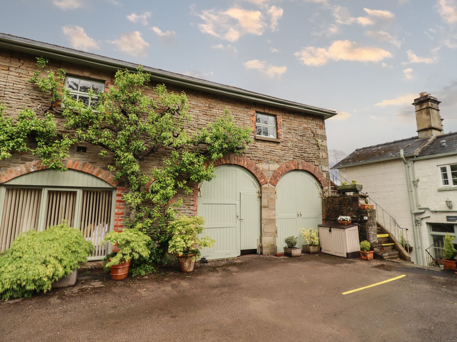 Stone building with green arched doors windows and various potted plants outside at The Carriage in Lydney