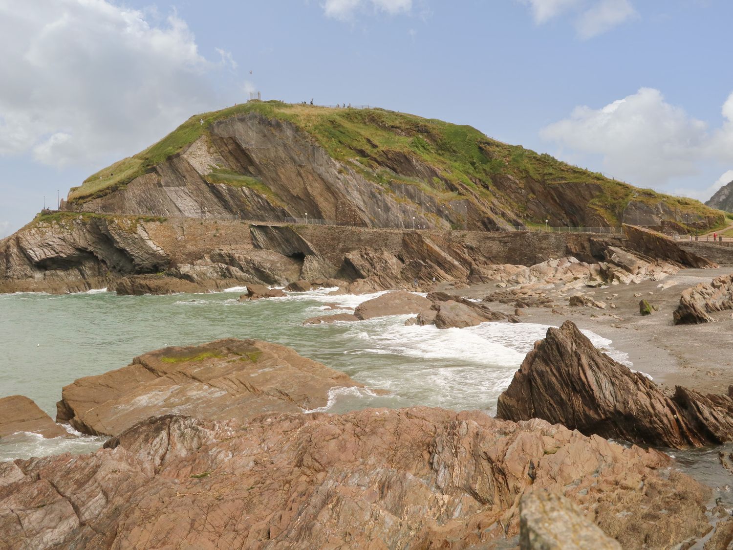 Rocky coastal area with a grassy hill and a stone wall along the shoreline at Torrs Walk View in Ilfracombe
