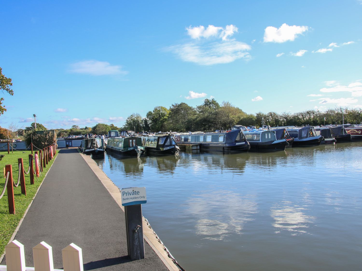 A marina with narrowboats moored along the water and a paved path beside the water at The Tyre Barn Whixall near Wem