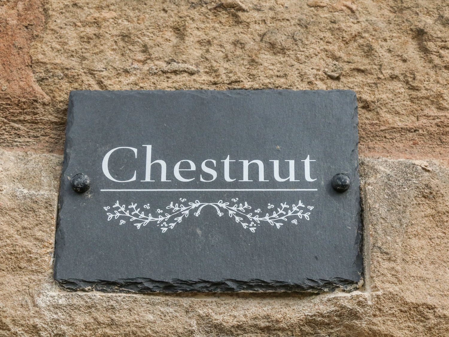 A dark stone plaque with the word Chestnut and decorative branches mounted on a stone wall at Chestnut Cottage in Stocksbridge