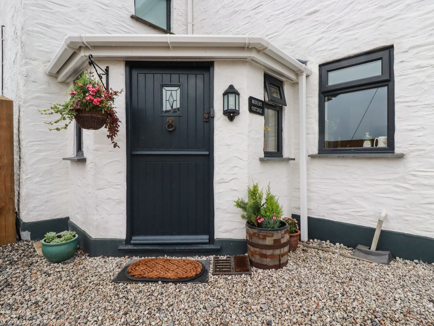A black door with a mat and flower pots outside at Miners cottage in St Austell