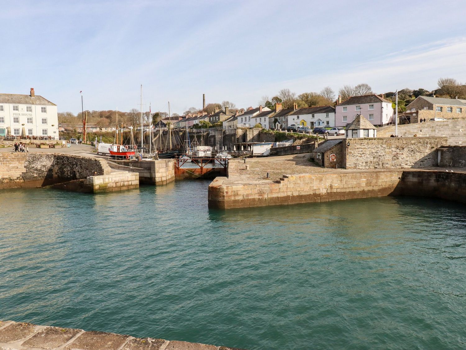 A harbor with boats docked near stone walls and buildings in the background at Miners cottage in St Austell