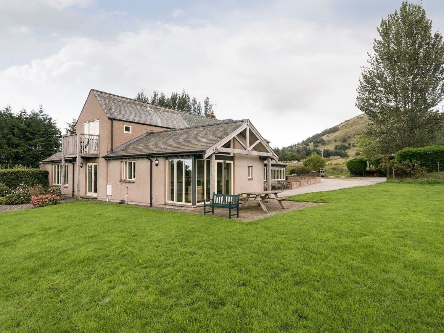 A house with a balcony and patio furniture on a lawn with trees and hills at Beckwood in Troutbeck near Keswick