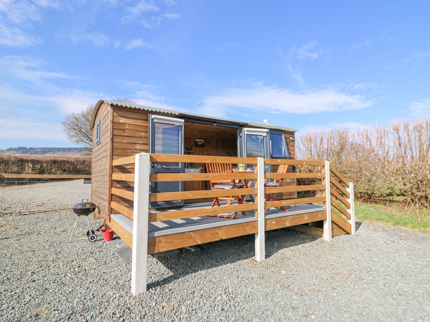 A small wooden cabin with a raised deck and outdoor furniture on a gravel area at Elan in Rhayader