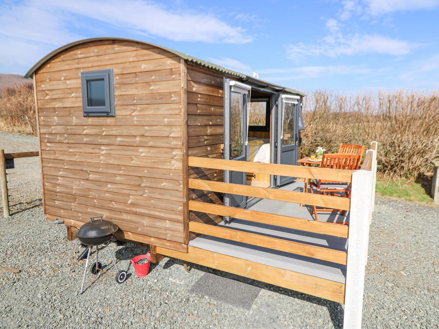 A small wooden cabin with an outdoor grilling area and patio furniture on a gravel surface at Elan in Rhayader