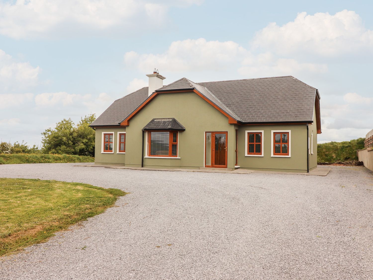 A green painted house with brown framed windows and gravel driveway at Daisys Cottage in Knockreagh near Listowel County Kerry