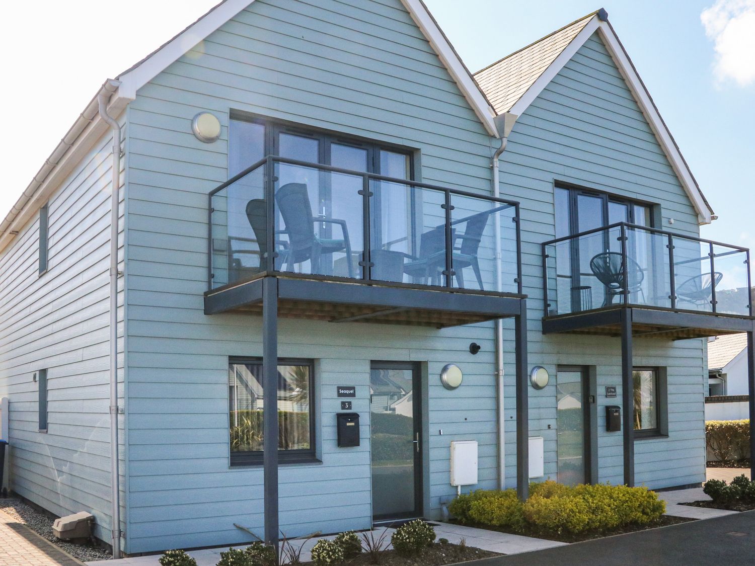 A two-story house with blue siding and glass balconies with chairs at Seaquel in Westward Ho