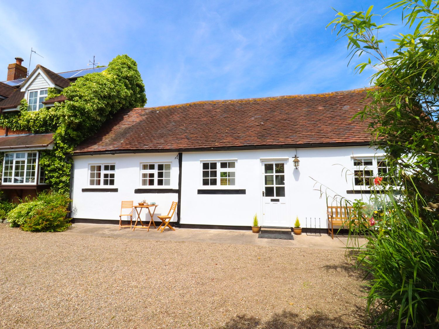 A white cottage with brown roof and outdoor seating surrounded by greenery at Mortons Cottage in Castlemorton near Malvern