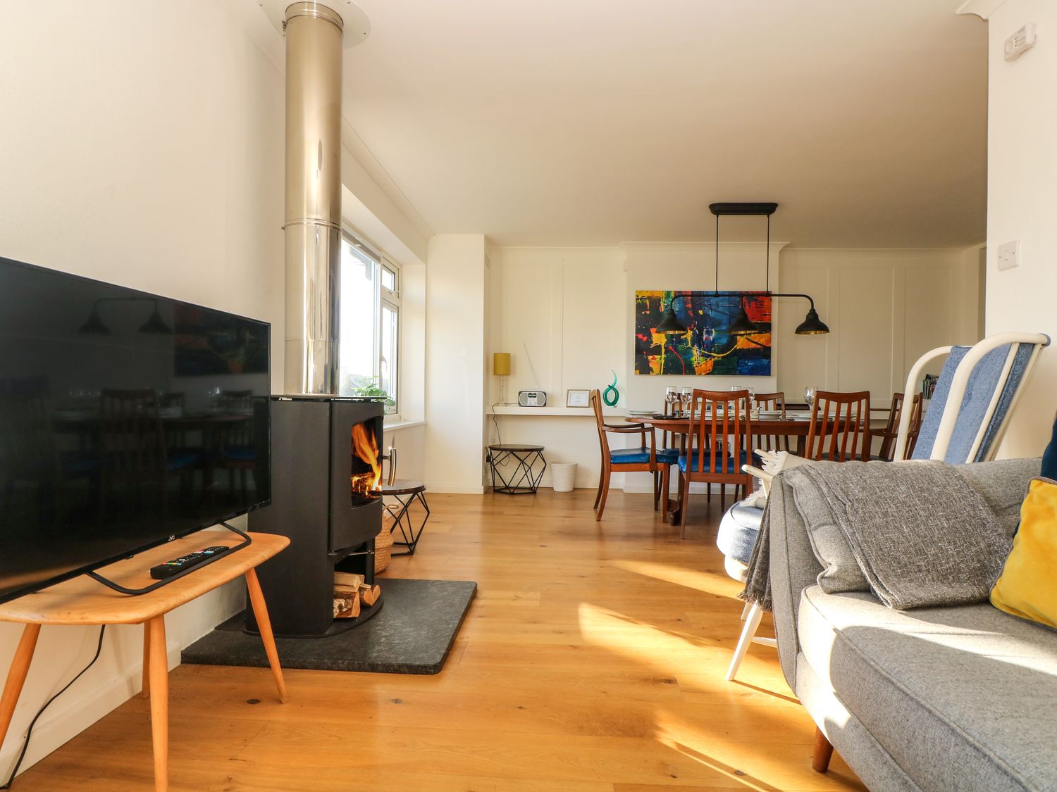 A living room with a wood stove television dining table and chairs at Rock Pool House in Porthleven