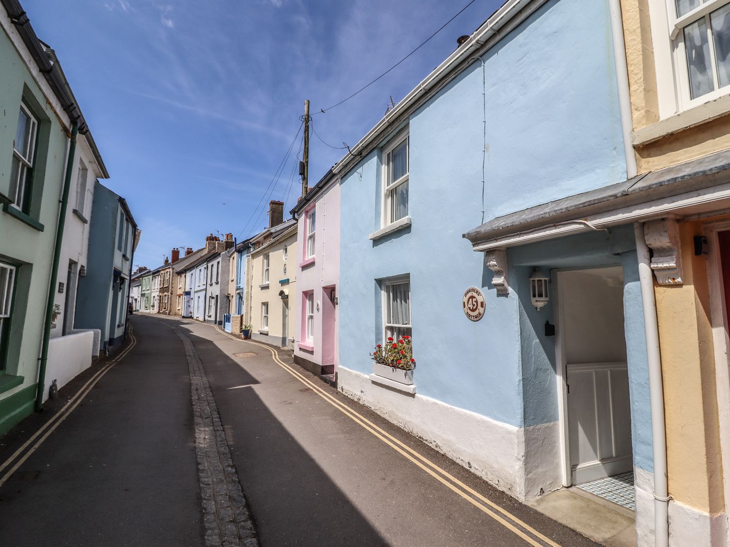 A narrow street with pastel colored houses and a blue house with an open door at Mariners Cottage in Appledore