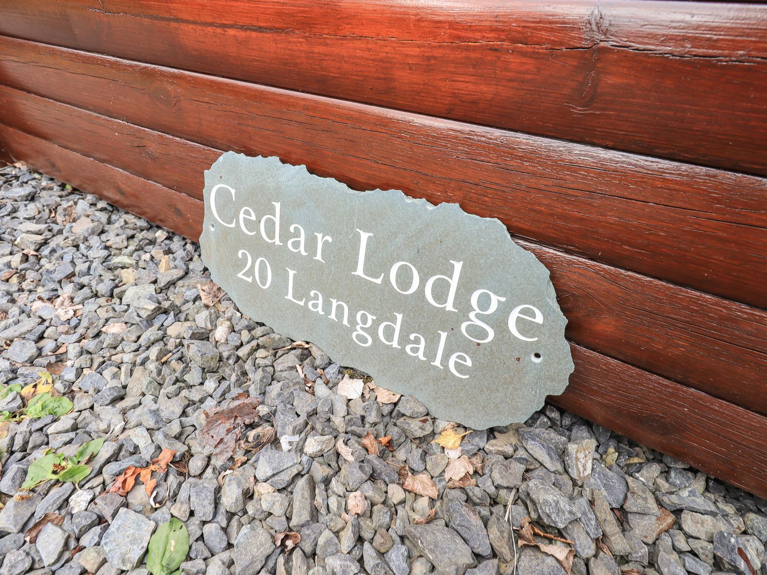 A sign reading Cedar Lodge 20 Langdale on gravel next to a wooden log wall at Cedar Lodge Langdale 20 White Cross Bay near Windermere